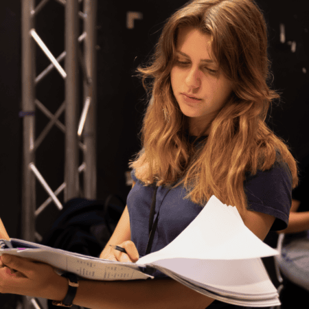 Jeune femme concentrée lisant et annotant des documents sur un plateau de tournage.