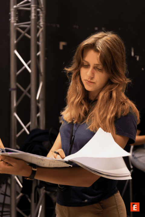 Jeune femme concentrée lisant et annotant des documents sur un plateau de tournage.