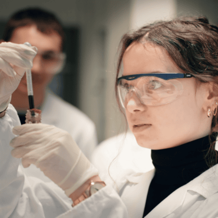 Jeune technicienne de laboratoire manipulant une pipette et un échantillon, gants et lunettes.