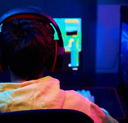 Gamer en sweat jaune devant écran PC, casque gaming, tour PC LED, ambiance cyberpunk.