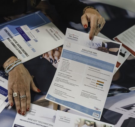 Mains feuilletant brochures Executive MBA et documents marketing, comparatif de programmes et statistiques.
