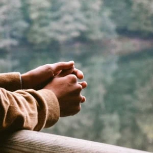 Mains entrelacées sur rambarde en bois au bord de leau, pull camel, ambiance sereine.