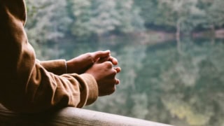 Mains entrelacées sur rambarde en bois au bord de leau, pull camel, ambiance sereine.