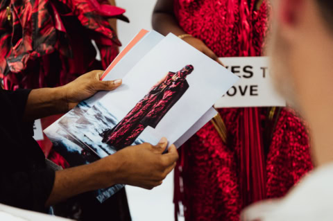 Mains tenant tirages mode rouges, photo manteau au bord de mer, tissus et textures.