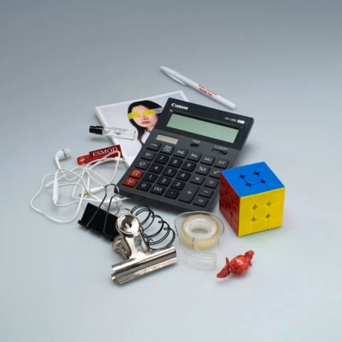 Objets de bureau : calculatrice Canon, cube puzzle coloré, écouteurs, ruban adhésif et clips.