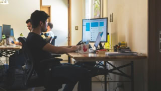 Open space bureau avec personne à lordinateur, écran, laptop, smartphone et accessoires de bureau.