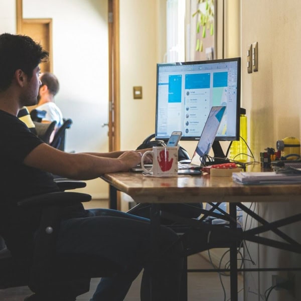 Open space bureau avec personne à lordinateur, écran, laptop, smartphone et accessoires de bureau.