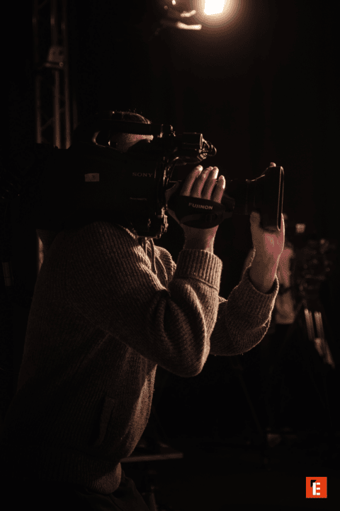 Opérateur caméra Sony Fujinon professionnel en studio, gros plan mains, éclairage dramatique.