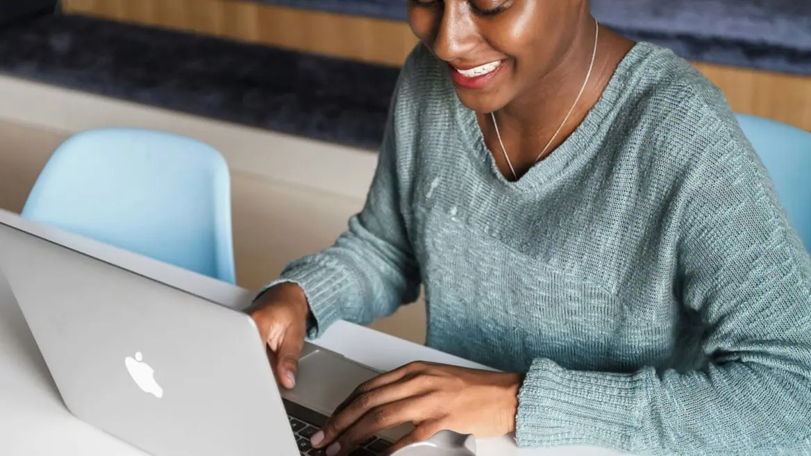 Personne travaillant sur MacBook portable à son bureau, clavier et souris.