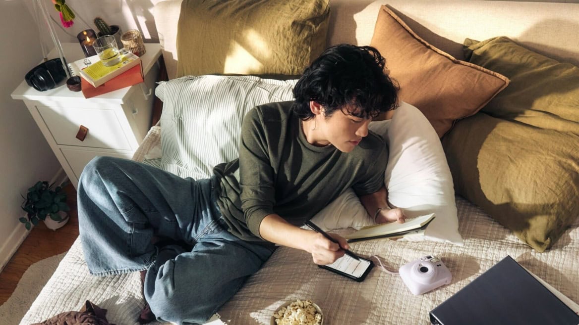 Personne écrivant sur lit avec carnet, téléphone et accessoires créatifs.