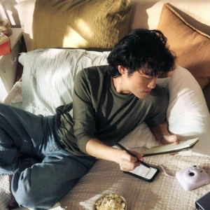 Personne écrivant sur lit avec carnet, téléphone et accessoires créatifs.