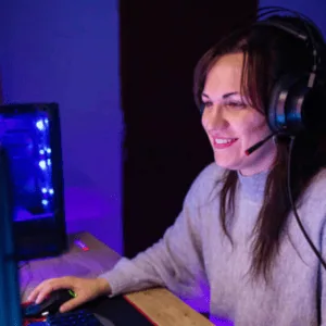 Personne en casque-micro devant PC gaming LED, clavier et souris sur bureau.