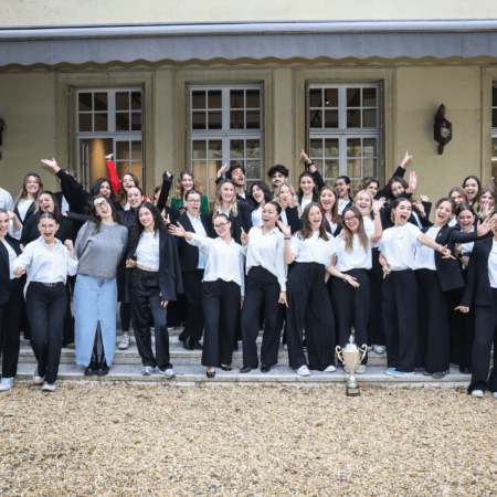 Photo de groupe déquipe célébrant une victoire avec trophée sur des marches devant bâtiment.