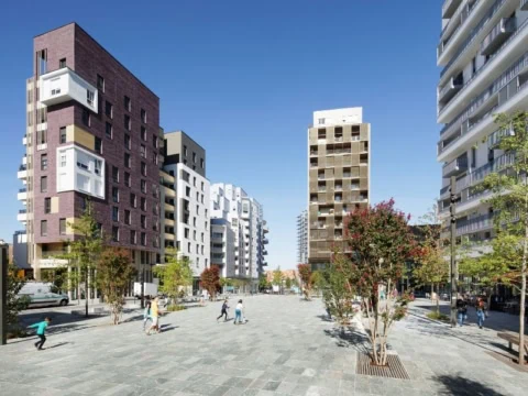 Place urbaine ensoleillée avec tours et logements résidentiels, arbres et piétons.