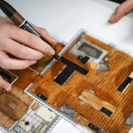 Mains dessinant et coloriant un plan détage architectural au feutre.