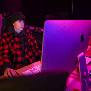 Portrait dune personne concentrée devant un iMac dans un studio créatif à léclairage violet.