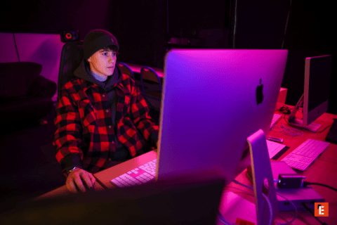 Portrait dune personne concentrée devant un iMac dans un studio créatif à léclairage violet.