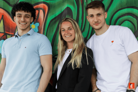 Portrait de groupe : trois jeunes souriants devant un graffiti coloré.