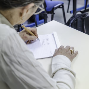 Prise de notes à crayon : mains âgées écrivant dans un carnet en classe.