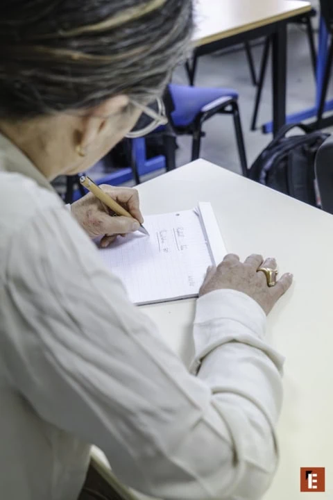 Prise de notes à crayon : mains âgées écrivant dans un carnet en classe.