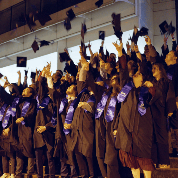 Remise de diplômes nocturne : étudiants en toges lançant leurs toques sur des marches.