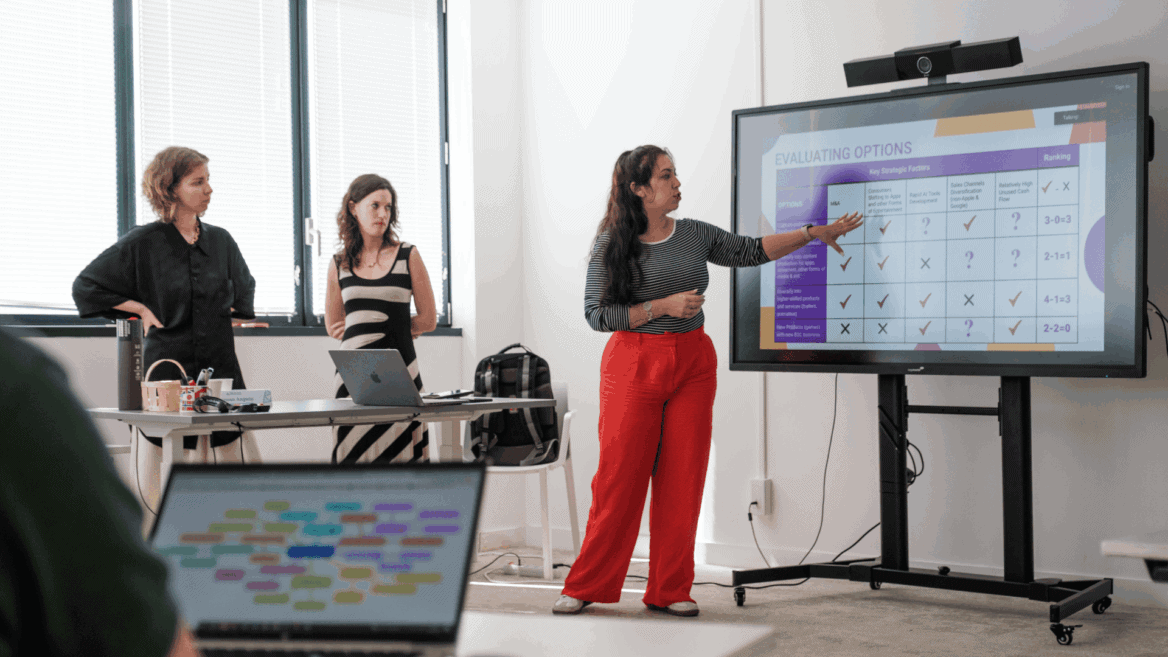 Réunion déquipe : trois femmes présentant un tableau dévaluation sur grand écran.