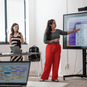 Réunion déquipe : trois femmes présentant un tableau dévaluation sur grand écran.