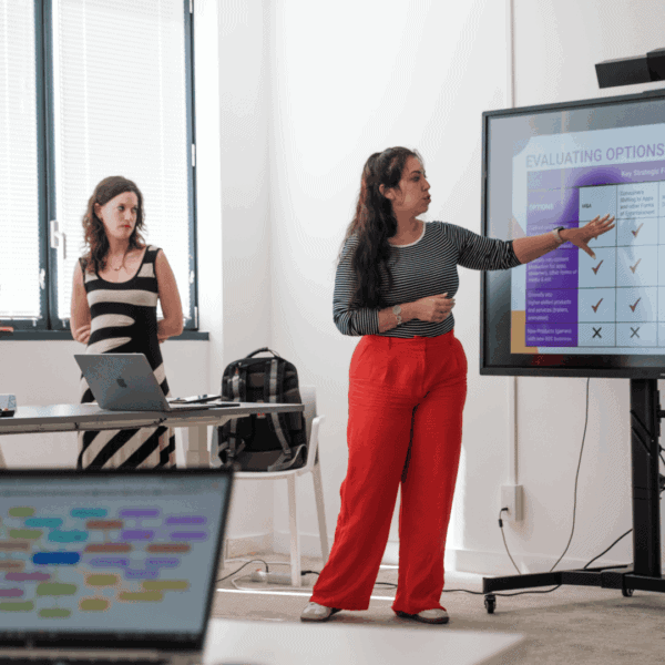 Réunion déquipe : trois femmes présentant un tableau dévaluation sur grand écran.