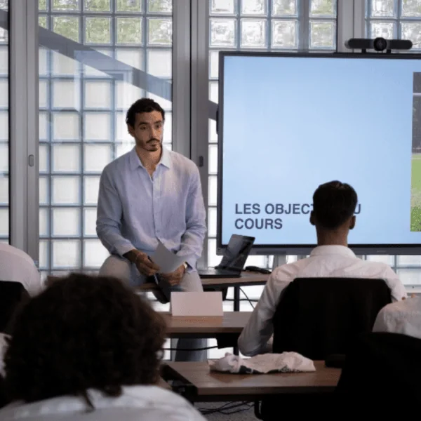 Réunion de formation en salle avec présentateur, écran, participants, coaching sportif et visioconférence.
