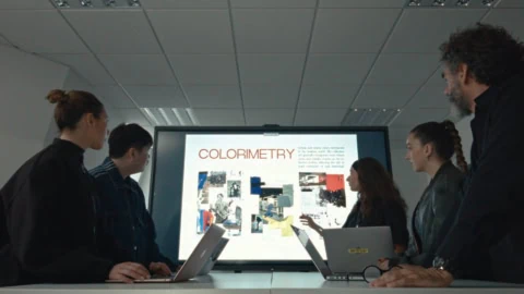 Réunion déquipe en salle, présentation colorimétrie sur grand écran, participants concentrés.