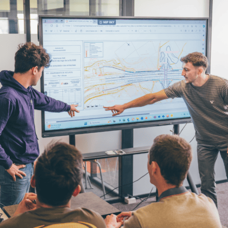 Réunion technique devant écran interactif affichant plan dinfrastructure, bureau moderne collaboratif.