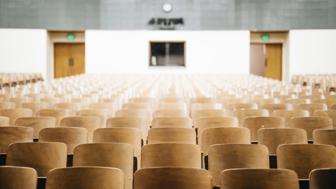 Salle de cours vide, rangées de sièges en bois en perspective.