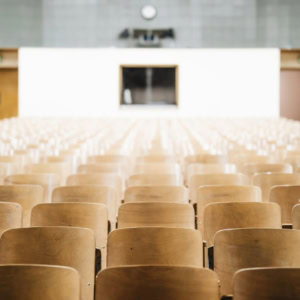 Salle de cours vide, rangées de sièges en bois en perspective.