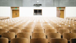 Salle de cours vide, rangées de sièges en bois en perspective.