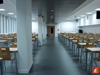 Salle dexamen vide avec rangées de bureaux et chaises en bois, fenêtres et lumière naturelle.