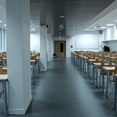 Salle dexamen vide avec rangées de bureaux et chaises en bois, fenêtres et lumière naturelle.