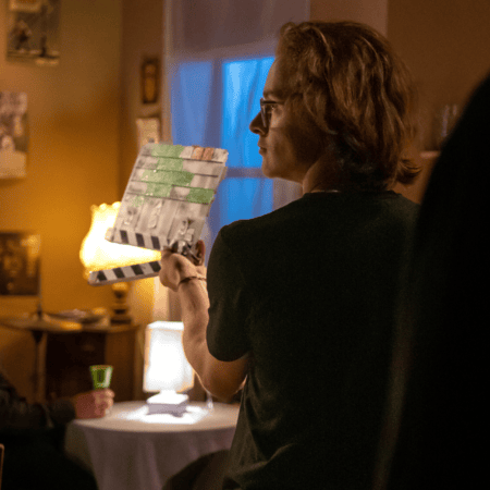 Personne en profil tenant un clap sur plateau de tournage intérieur, lumières chaudes et bleues.