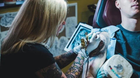 Séance de tatouage poitrine : tatoueuse professionnelle au travail en studio, machine visible.