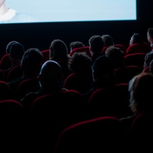 Spectateurs dans une salle de cinéma aux sièges rouges, écran lumineux.