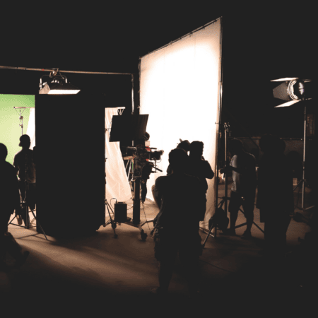 Studio de tournage avec écran vert, grande diffusion lumineuse, équipe technique et caméra en silhouette.
