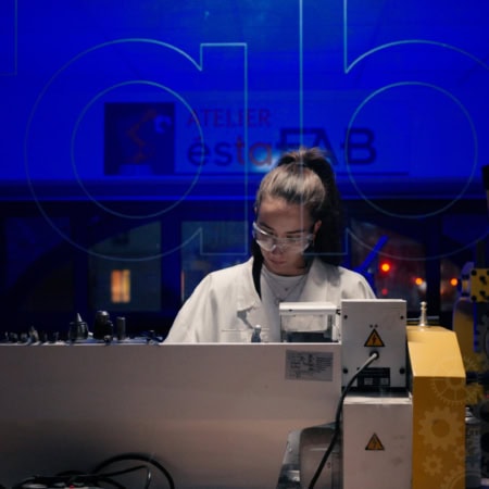 Technicien en blouse blanche travaillant sur machine industrielle dusinage dans atelier éclairé en bleu.