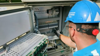 Technicien inspectant panneau électrique industriel ouvert, maintenance câblage sécurisé, casque et gants.