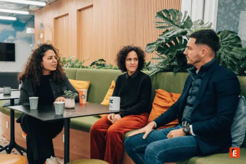 Trois personnes en réunion informelle sur canapé vert, plantes, café et ambiance collaborative.