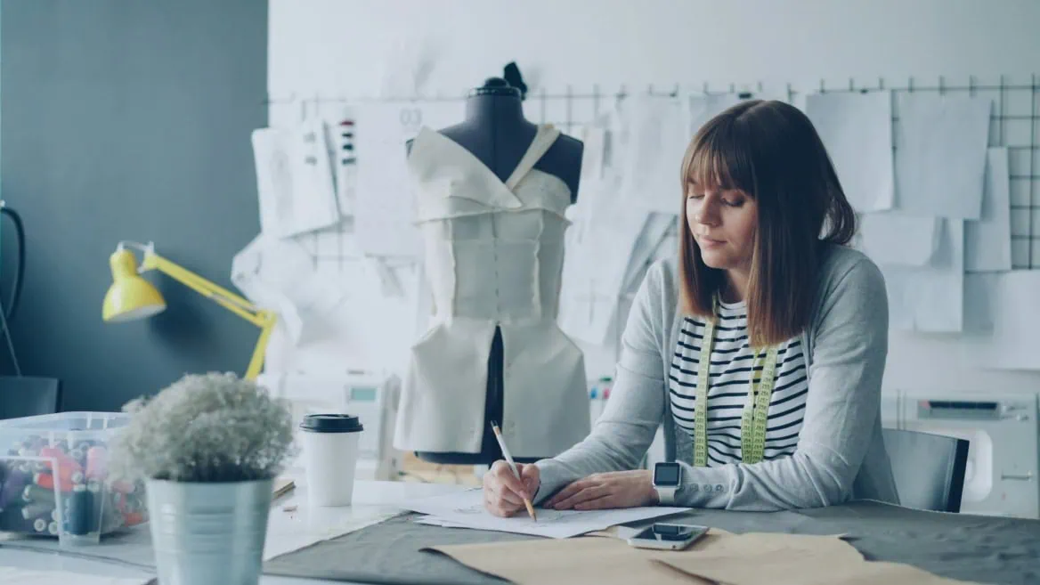 Femme en atelier couture dessinant un patron près d’un mannequin.