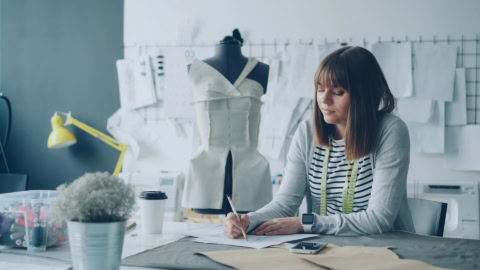 Femme en atelier couture dessinant un patron près d’un mannequin.