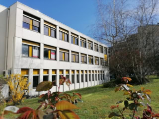 Bâtiment moderne trois étages façade blanche, fenêtres jaunes, pelouse et arbres.
