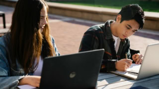 Étudiants travaillant dehors avec ordinateurs portables et cahiers, prise de notes au soleil.