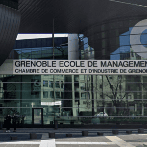 Façade de Grenoble École de Management en verre avec toit incliné et logo bleu.