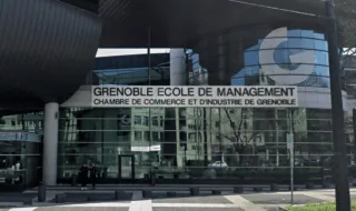 Façade de Grenoble École de Management en verre avec toit incliné et logo bleu.