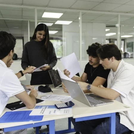 Groupe détudiants en salle détude collaborant autour dune table avec ordinateurs et documents.